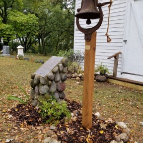 Photo of a church bell on a post in front of the church